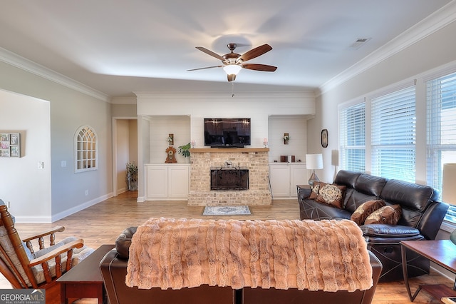 living room with a brick fireplace, ceiling fan, light hardwood / wood-style flooring, and ornamental molding