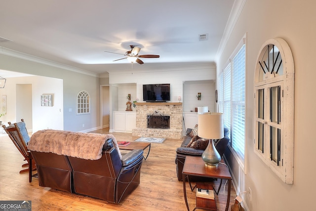 living room with ornamental molding, light hardwood / wood-style floors, a wealth of natural light, and a stone fireplace