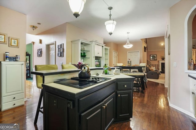 kitchen featuring black stovetop, decorative light fixtures, a kitchen island, dark hardwood / wood-style flooring, and a breakfast bar area