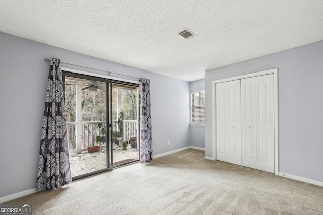 unfurnished bedroom with access to exterior, carpet floors, a textured ceiling, and a closet