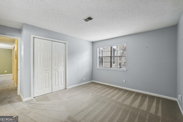 unfurnished bedroom featuring light colored carpet, a textured ceiling, and a closet