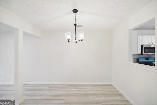 dining area with light wood-type flooring, a textured ceiling, and a chandelier