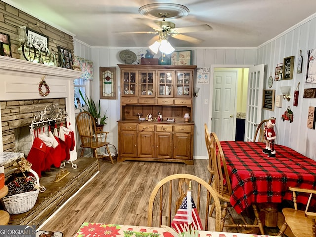 dining space featuring hardwood / wood-style flooring, a stone fireplace, ceiling fan, and ornamental molding