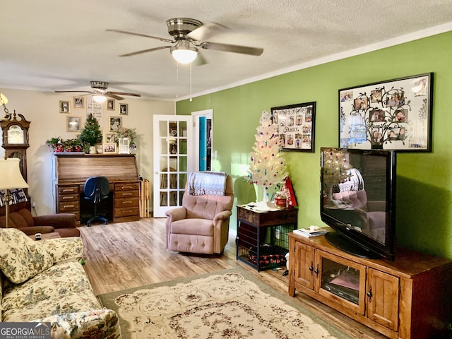 living room featuring ceiling fan, crown molding, light wood-type flooring, and a textured ceiling