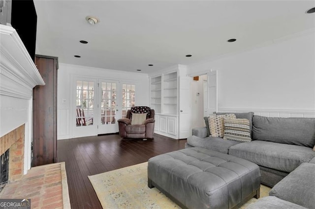 living room featuring built in shelves, dark hardwood / wood-style flooring, and a fireplace