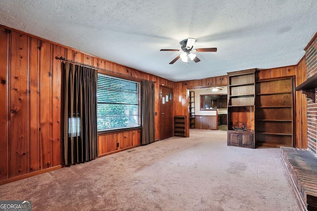 unfurnished living room with ceiling fan, wood walls, carpet floors, and a textured ceiling