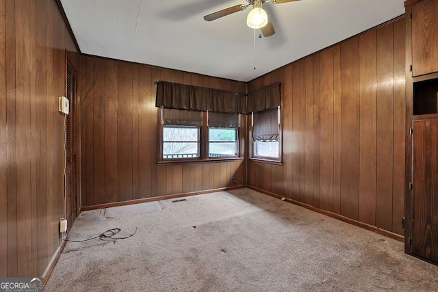 carpeted empty room featuring wood walls and ceiling fan