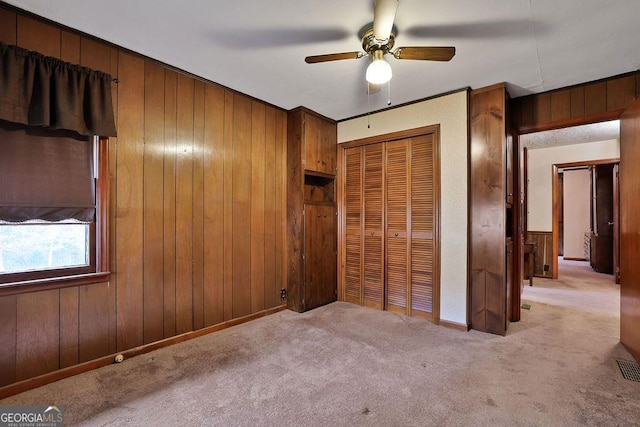 unfurnished bedroom featuring a closet, light colored carpet, ceiling fan, and wood walls