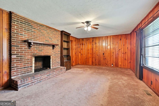 unfurnished living room with wood walls, a fireplace, ceiling fan, and light colored carpet