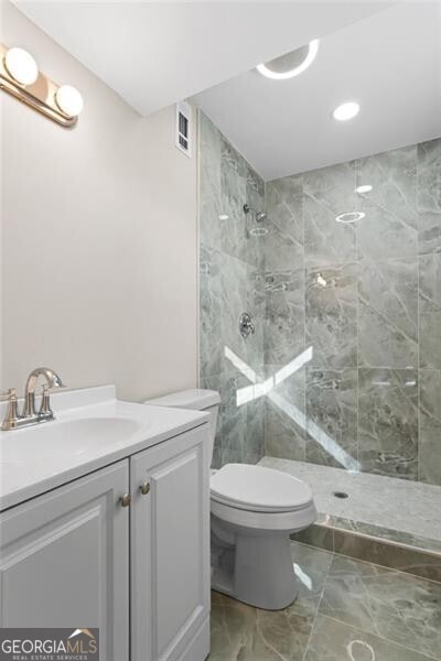 bathroom featuring vanity, toilet, and a tile shower