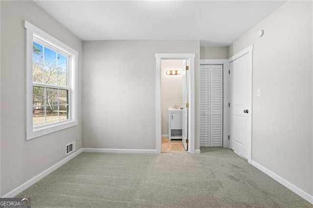 unfurnished bedroom featuring light carpet and ensuite bath