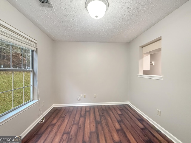 empty room featuring plenty of natural light, dark wood-type flooring, and a textured ceiling