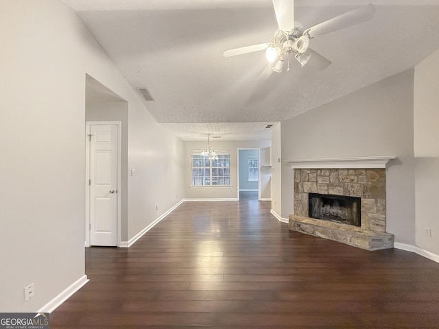 unfurnished living room with ceiling fan with notable chandelier, a stone fireplace, vaulted ceiling, a textured ceiling, and dark hardwood / wood-style flooring