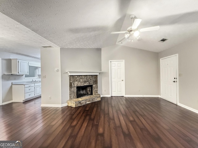 unfurnished living room with lofted ceiling, a stone fireplace, sink, dark hardwood / wood-style floors, and ceiling fan