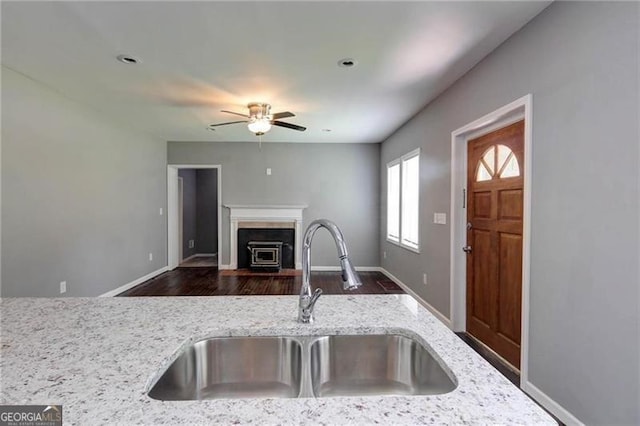 kitchen with light stone counters, sink, ceiling fan, and dark wood-type flooring