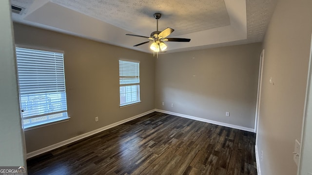 empty room with a raised ceiling, ceiling fan, dark wood-type flooring, and a healthy amount of sunlight