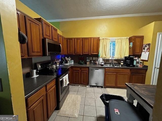 kitchen with brown cabinets, light tile patterned floors, dark countertops, appliances with stainless steel finishes, and a sink