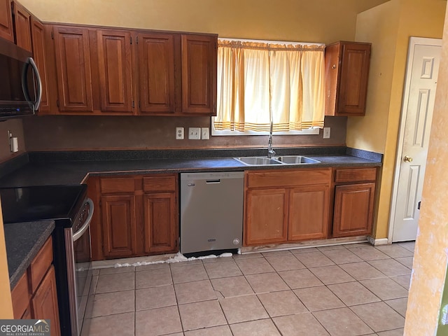 kitchen with brown cabinets, light tile patterned floors, dark countertops, appliances with stainless steel finishes, and a sink