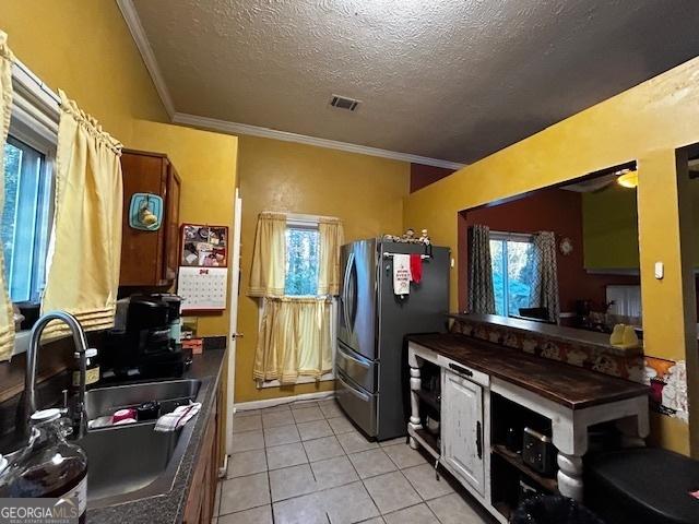 kitchen featuring light tile patterned flooring, a sink, visible vents, freestanding refrigerator, and dark countertops