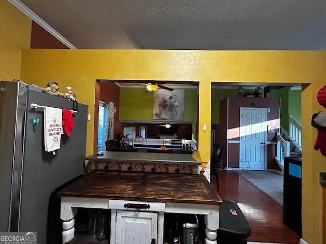 kitchen with ornamental molding, freestanding refrigerator, ceiling fan, a textured ceiling, and wood finished floors