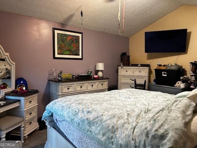 bedroom with dark colored carpet, vaulted ceiling, and a textured ceiling