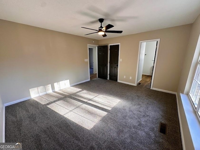 unfurnished bedroom with a walk in closet, ceiling fan, and dark carpet