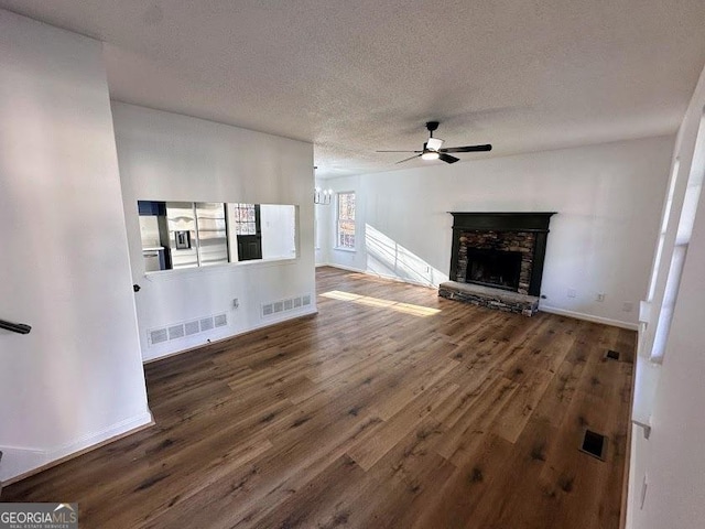 unfurnished living room featuring a textured ceiling, a stone fireplace, ceiling fan with notable chandelier, and dark hardwood / wood-style floors