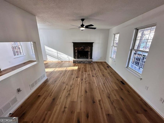 unfurnished living room featuring a stone fireplace, ceiling fan, hardwood / wood-style floors, and a textured ceiling