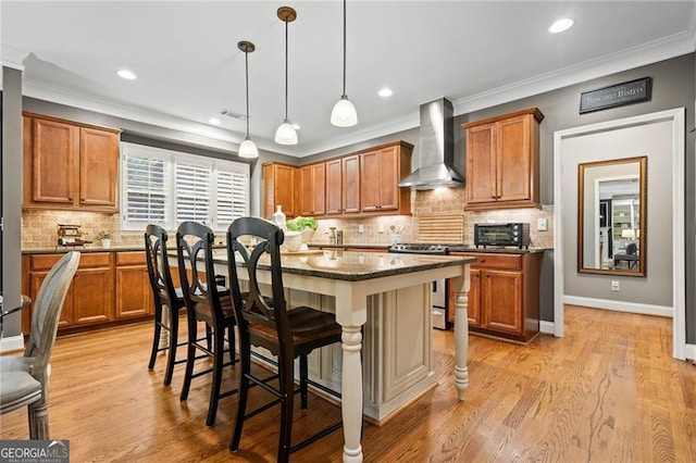 kitchen with a breakfast bar, wall chimney range hood, stainless steel gas range, a kitchen island, and light hardwood / wood-style floors