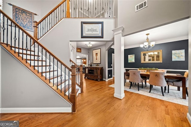 foyer entrance with a towering ceiling, decorative columns, ornamental molding, an inviting chandelier, and light hardwood / wood-style flooring