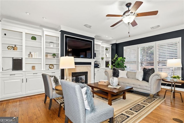 living room with crown molding, light hardwood / wood-style flooring, a high end fireplace, and ceiling fan