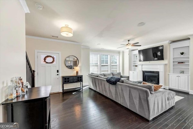 living room featuring ceiling fan, crown molding, dark wood-type flooring, and built in shelves