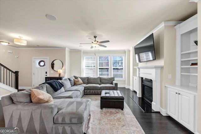 living room with built in shelves, crown molding, ceiling fan, and dark wood-type flooring