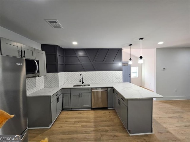 kitchen with sink, stainless steel appliances, kitchen peninsula, pendant lighting, and light hardwood / wood-style floors