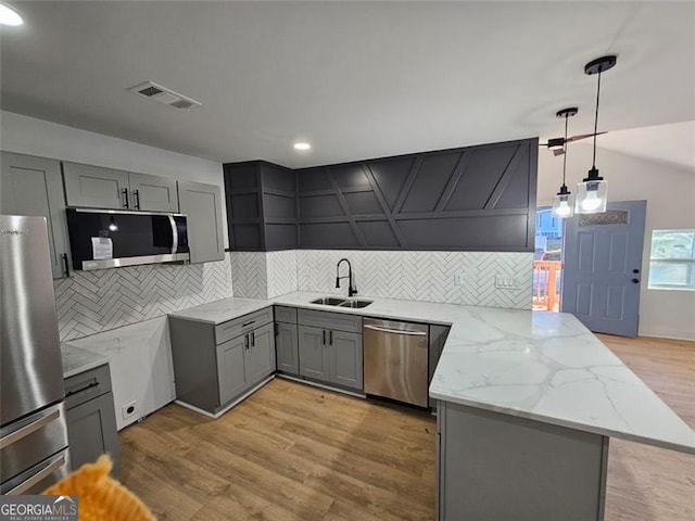 kitchen featuring kitchen peninsula, stainless steel appliances, sink, light hardwood / wood-style flooring, and hanging light fixtures