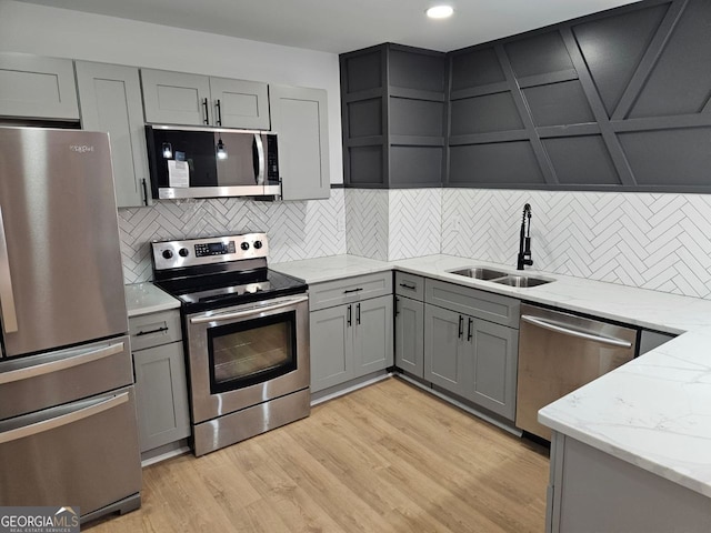 kitchen with sink, stainless steel appliances, tasteful backsplash, light stone counters, and light hardwood / wood-style flooring