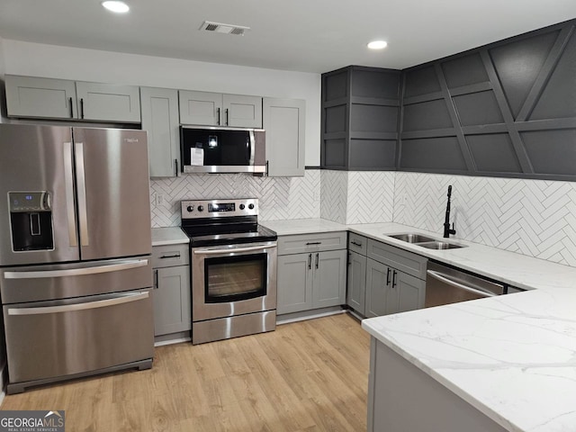 kitchen featuring gray cabinetry, sink, light stone countertops, light wood-type flooring, and stainless steel appliances