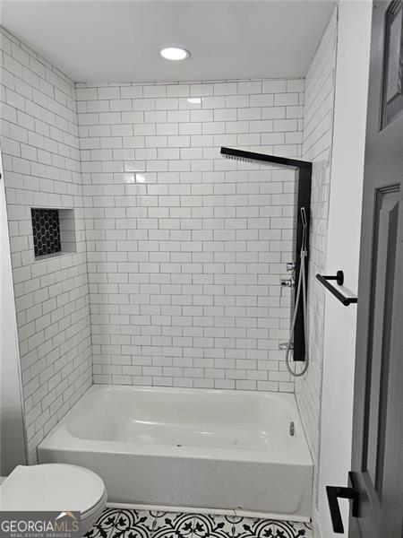 bathroom featuring tiled shower / bath combo and toilet