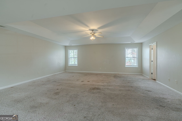 carpeted spare room featuring plenty of natural light, ceiling fan, and a tray ceiling