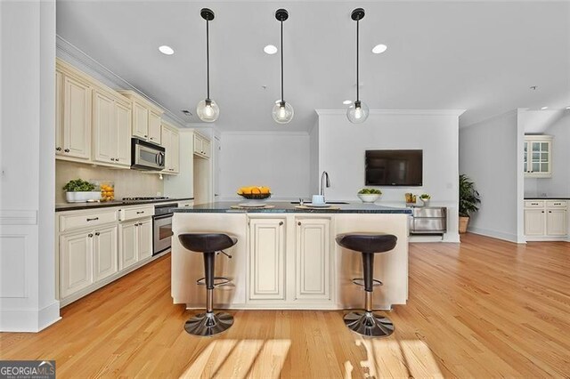 kitchen with a breakfast bar, light wood-type flooring, stainless steel appliances, and cream cabinets