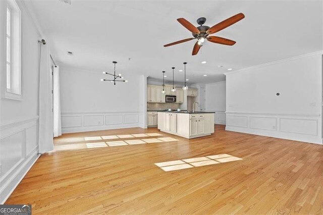 unfurnished living room with ceiling fan with notable chandelier, light hardwood / wood-style flooring, and ornamental molding