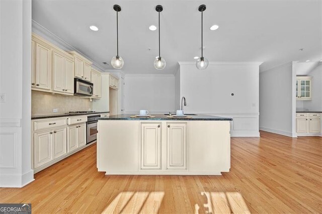 kitchen featuring appliances with stainless steel finishes, sink, decorative light fixtures, cream cabinetry, and light hardwood / wood-style floors