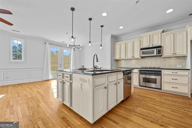 kitchen featuring a kitchen island with sink, sink, stainless steel appliances, and decorative light fixtures