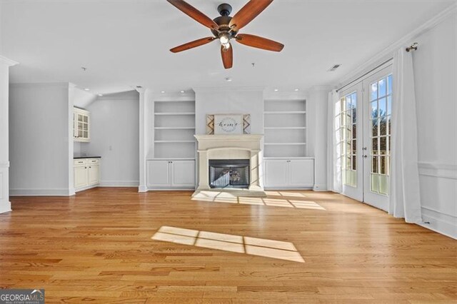 unfurnished living room featuring crown molding, french doors, light hardwood / wood-style floors, and built in features