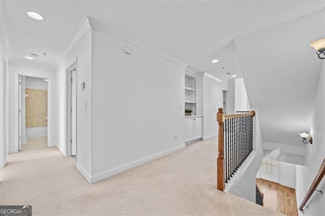 hallway featuring built in shelves, light colored carpet, and ornamental molding