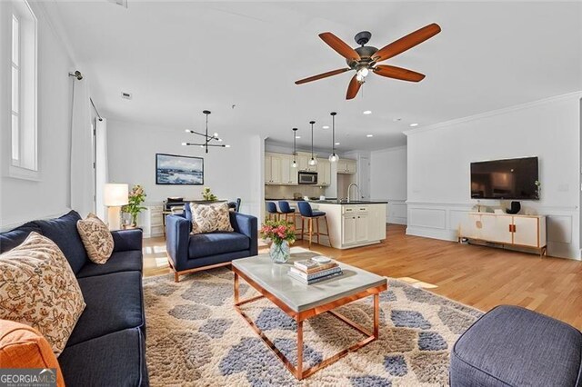 living room featuring ornamental molding, ceiling fan with notable chandelier, and light wood-type flooring