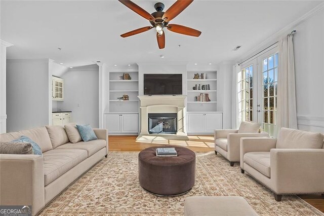 living room with french doors, hardwood / wood-style flooring, ceiling fan, built in shelves, and ornamental molding