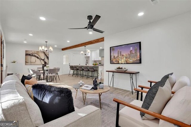 living room featuring beam ceiling, ceiling fan with notable chandelier, and light hardwood / wood-style floors