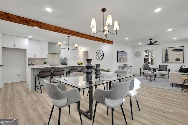 dining area featuring sink, beamed ceiling, ceiling fan with notable chandelier, and light wood-type flooring