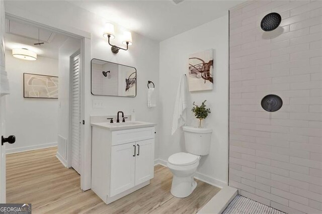 bathroom with hardwood / wood-style flooring, vanity, toilet, and a tile shower